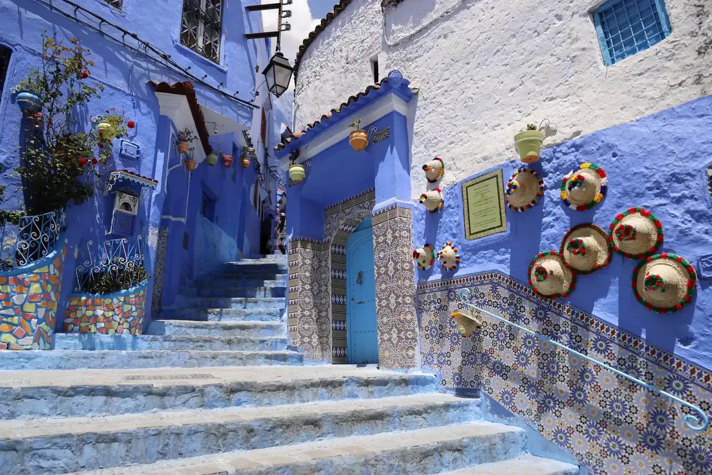 Blue-washed steps and a tiled doorway in the Chefchaouen medina, straw hats on the wall