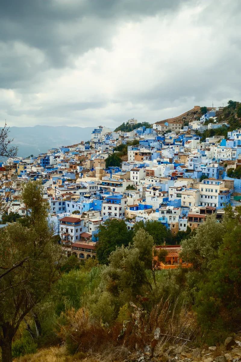 The blue houses of Chefchaouen climbing the Rif hillside under a grey sky
